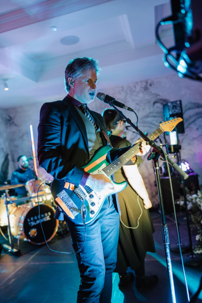 Live band performing with guitarist and singer under colorful stage lighting