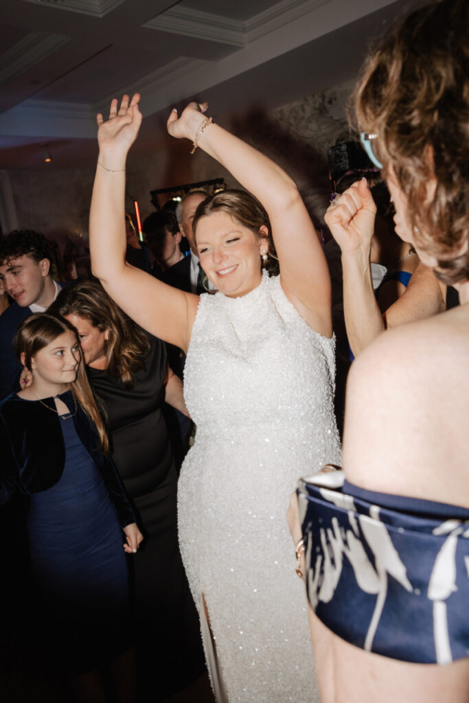 Bride dancing with arms raised surrounded by guests on the dance floor