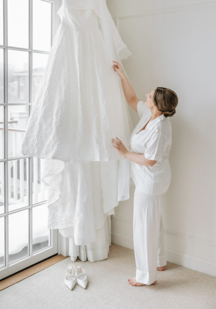 Bride adjusting wedding dress by window light, soft bridal detail styled by Newport wedding planner