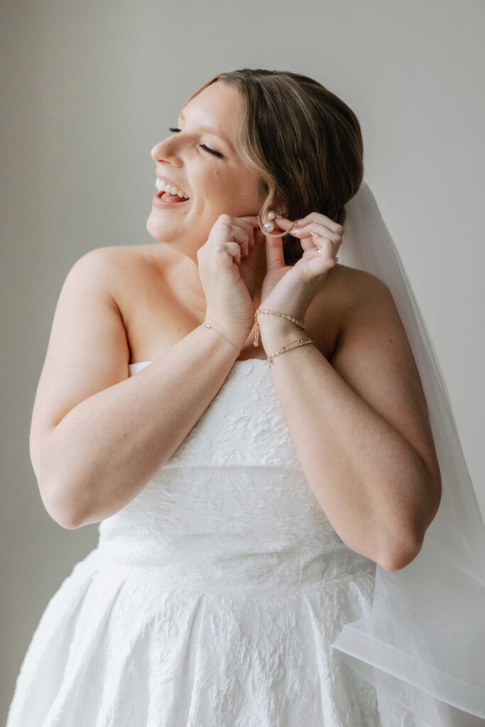 Bride putting on earrings, joyful getting ready moment during Newport wedding morning