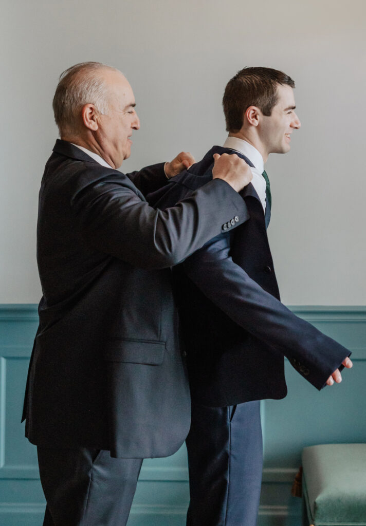 Groom’s father helping him into jacket, meaningful Newport wedding getting ready moment