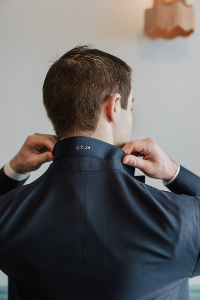 Close-up of groom adjusting jacket collar with embroidered date, personalized Newport wedding detail
