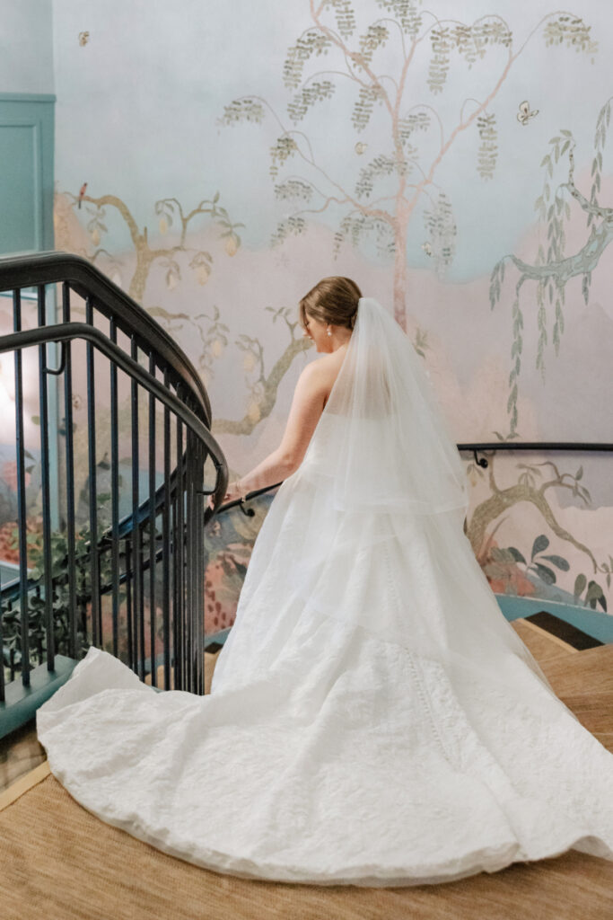 Bride walking staircase with long train and veil, mural backdrop at stylish Newport wedding venue