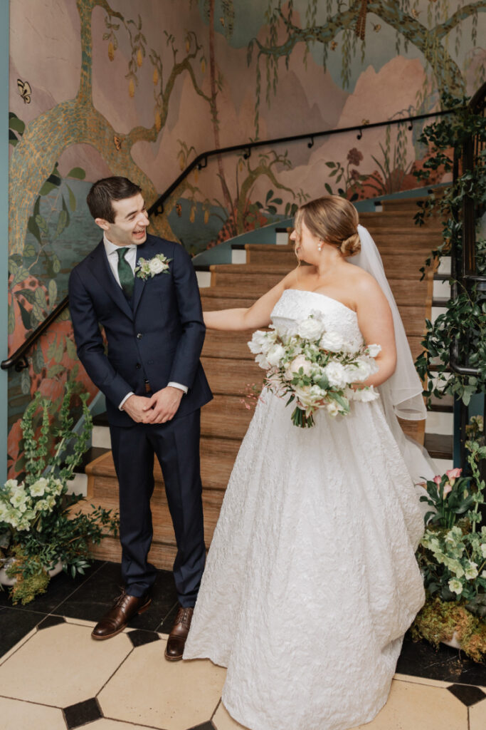 Bride and groom laughing during first look on staircase, mural backdrop at Newport wedding