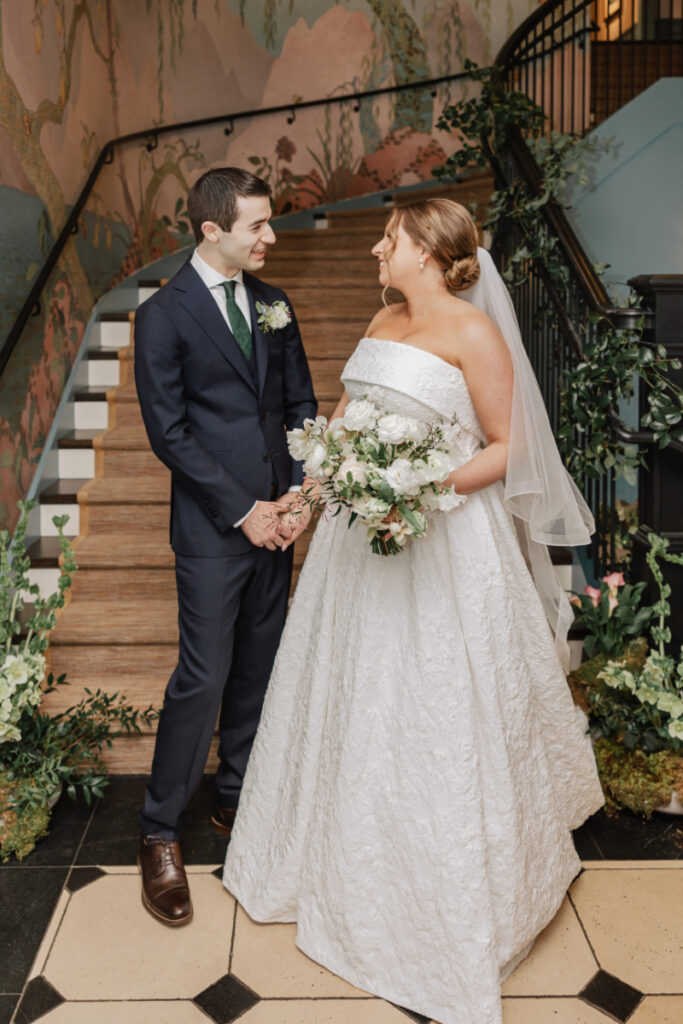 Bride and groom holding hands on staircase, romantic portrait with mural backdrop at Newport wedding