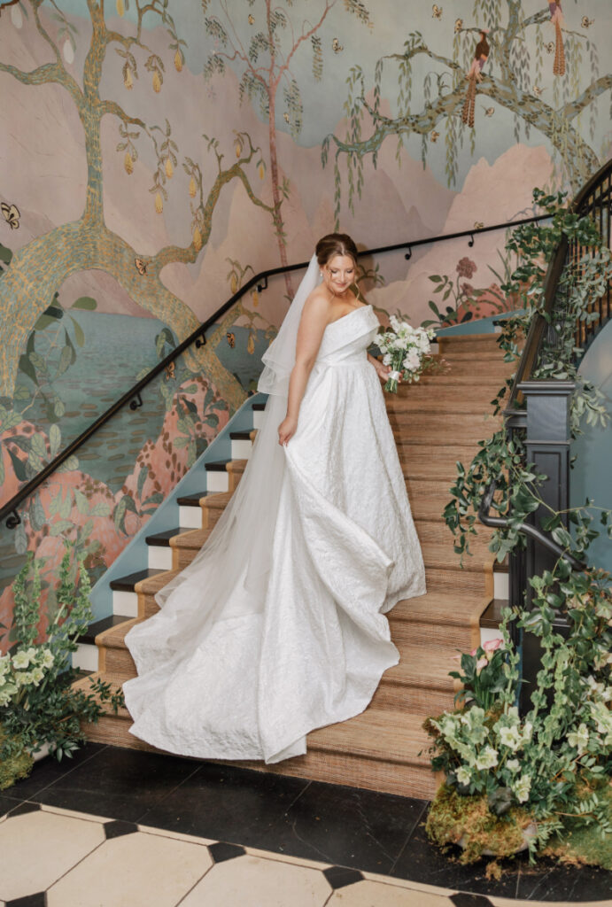 Bride walking down staircase with flowing gown and greenery, mural backdrop at Newport wedding