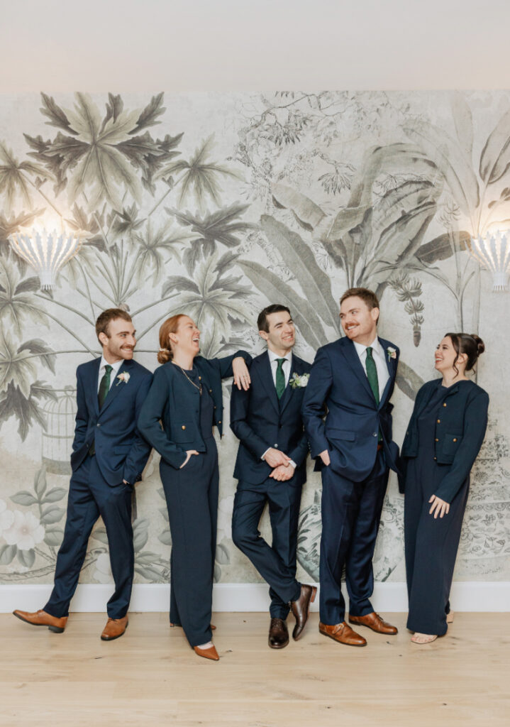 Groom and wedding party laughing together, candid moment against mural wall at Newport wedding