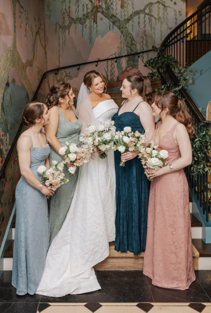 Bride with bridesmaids on staircase, soft pastel dresses and florals at Newport wedding