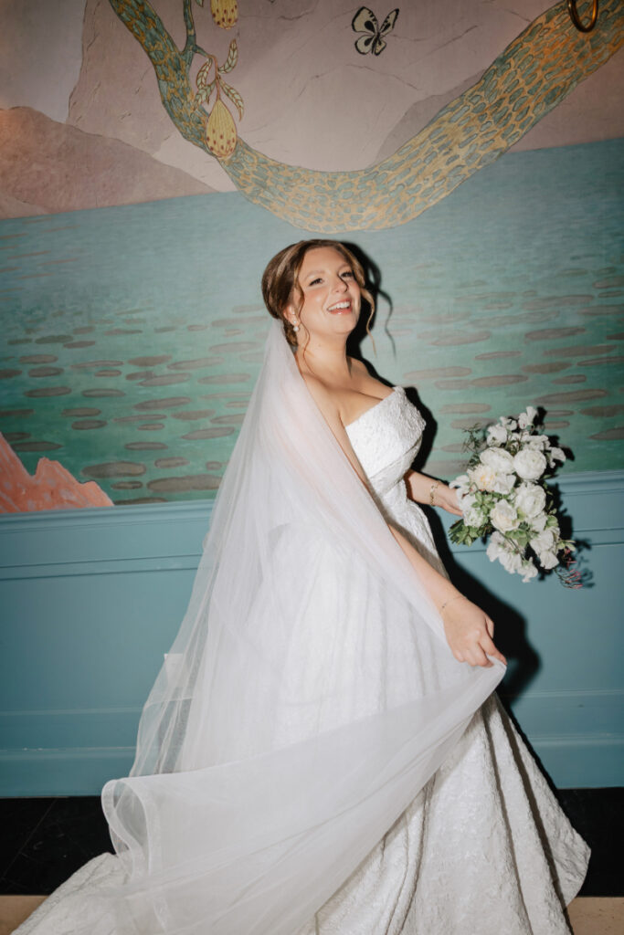 Bride twirling with veil and bouquet against mural wall, joyful candid moment at Newport wedding
