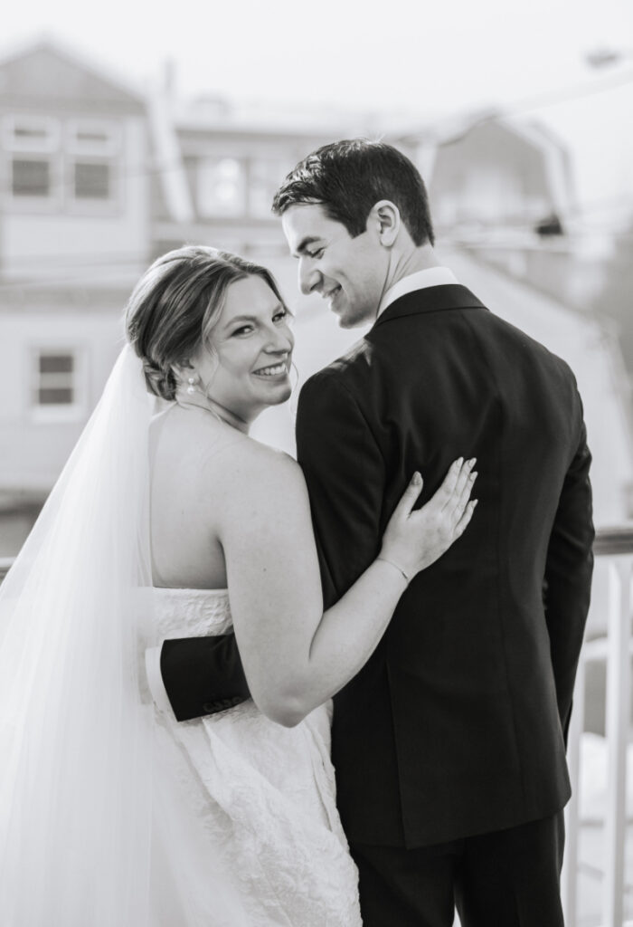 Black and white portrait of couple embracing on balcony, candid moment overlooking Newport wedding setting
