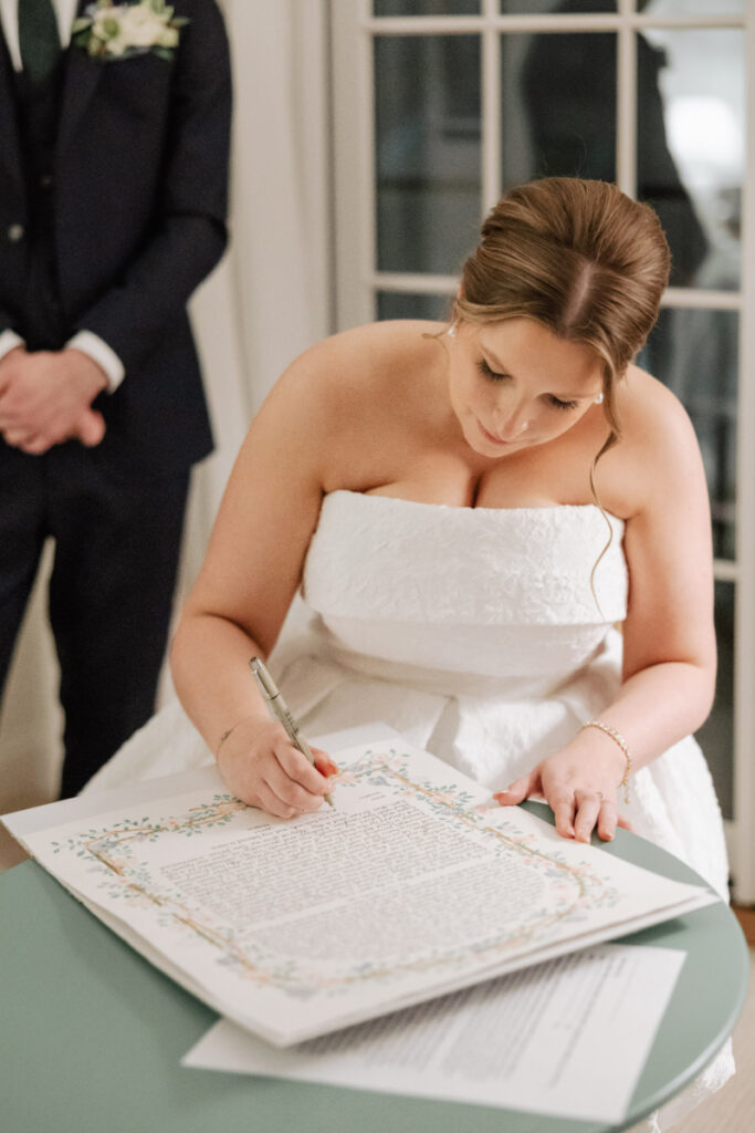 Bride signing ketubah with focused expression, meaningful ceremony moment captured up close