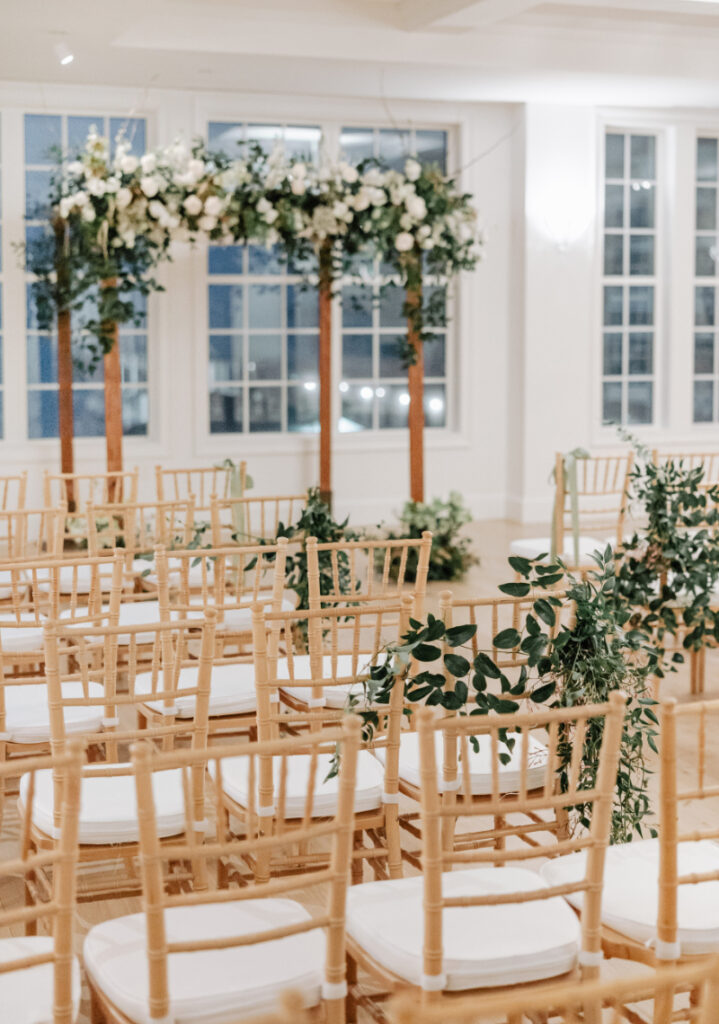 Chiavari chairs and greenery-lined aisle facing floral arch, classic indoor Newport wedding ceremony setting