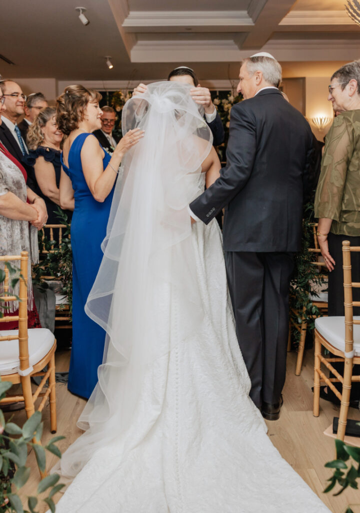 Parents lifting veil over bride during ceremony, emotional moment surrounded by smiling guests