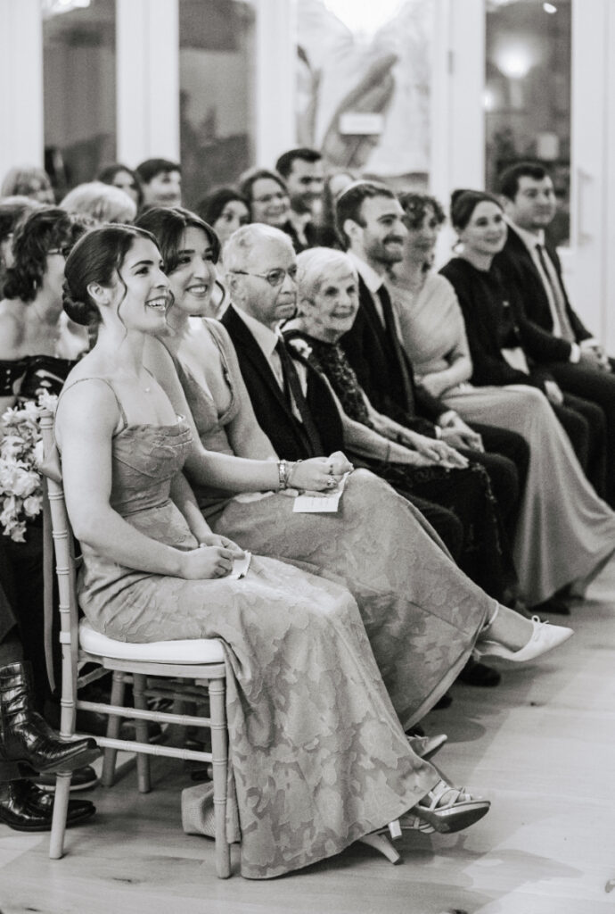 Guests seated during ceremony, smiling and engaged, candid reactions captured throughout meaningful moment