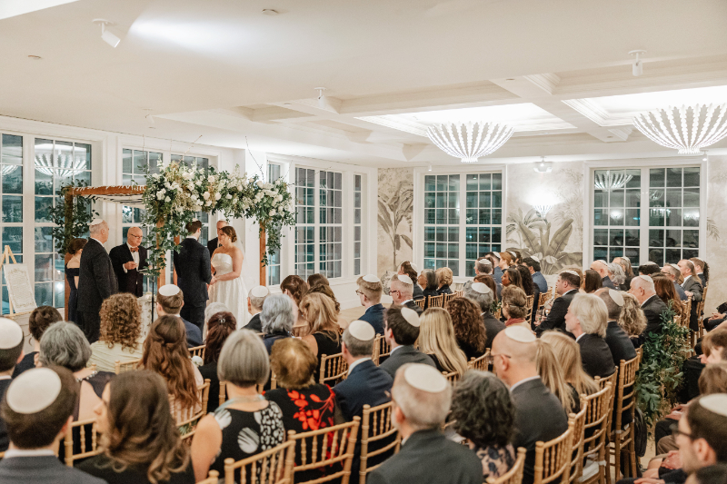 Wide ceremony view with guests seated and couple at altar, full room perspective during vows