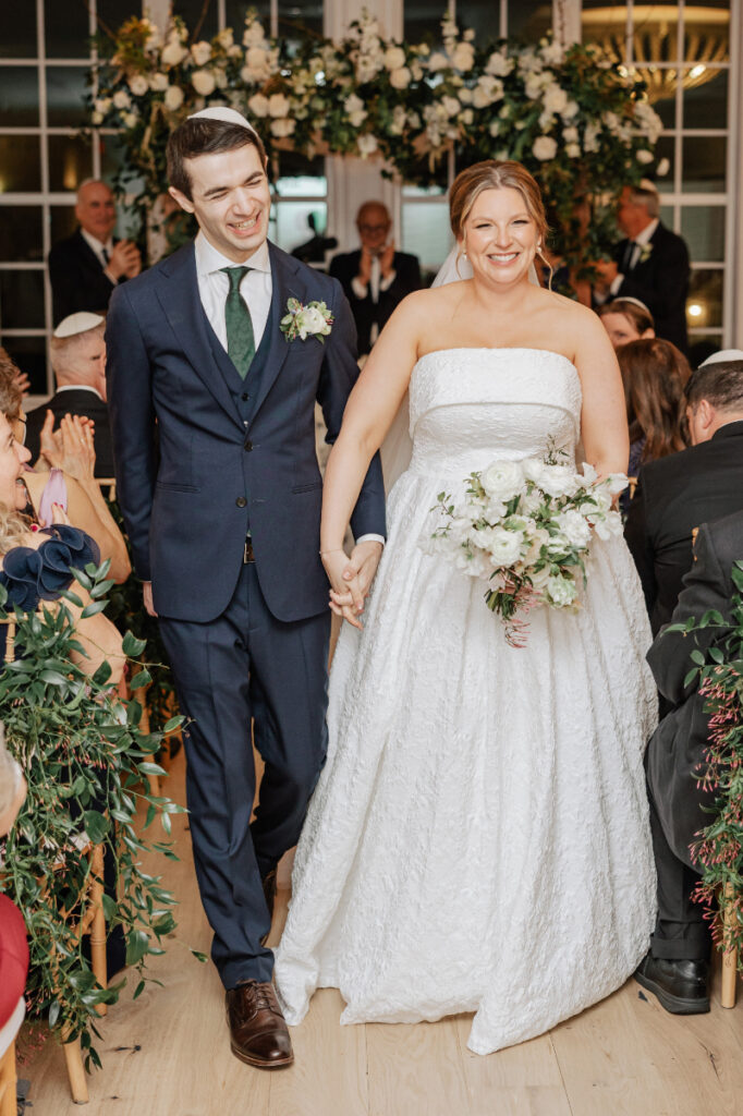 Newlyweds walking down aisle smiling, joyful recessional moment as guests celebrate around them