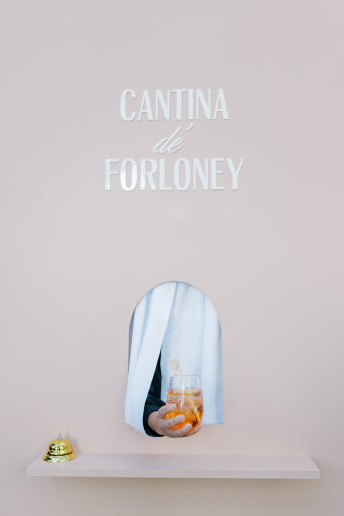 Minimalist bar setup with a hidden service window passing a cocktail through a soft, neutral backdrop