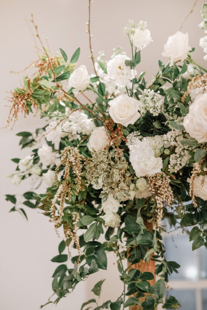 Lush white and green floral arrangement with roses, greenery, and textured blooms for romantic wedding design