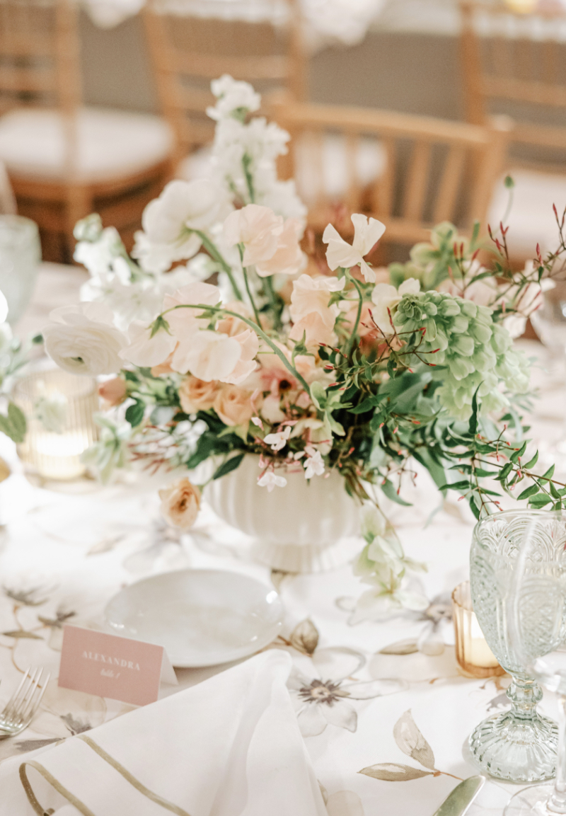 Soft pastel floral centerpiece with mixed blooms and greenery on patterned table for romantic wedding reception design