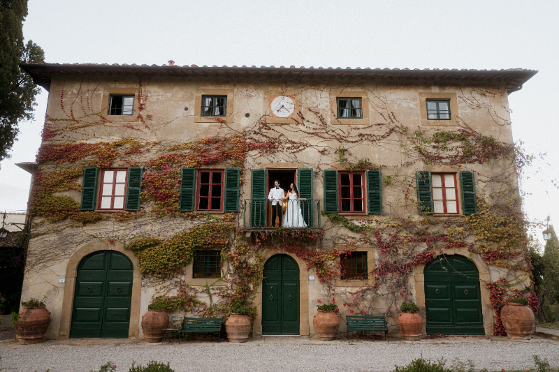 Couple standing on balcony of ivy-covered villa with rustic charm and countryside setting